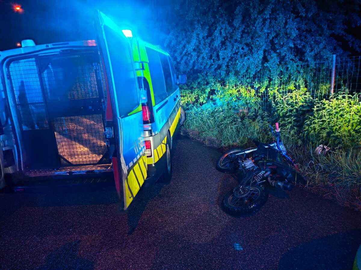 Nocna ucieczka motocyklisty Szczecinek zakończona pościgiem, policyjne radiowozy blokujące ulicę i zatrzymany agresywny kierowca na chodniku.